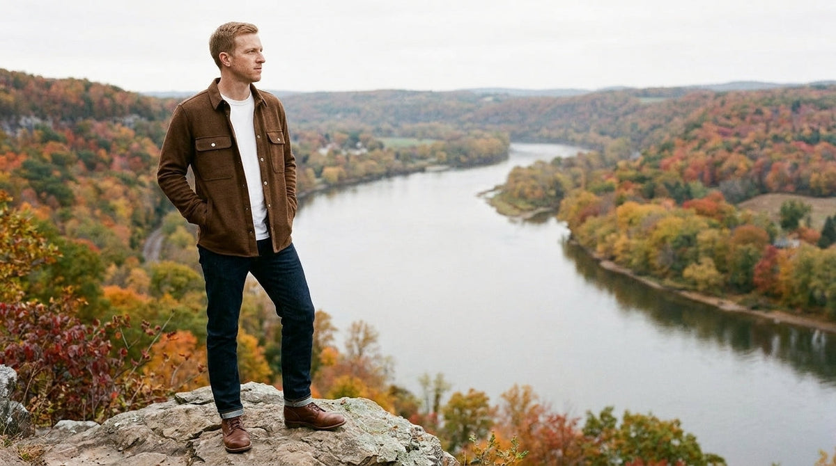 Man in a brown shirt jacket over a white tee at an autumn river overlook