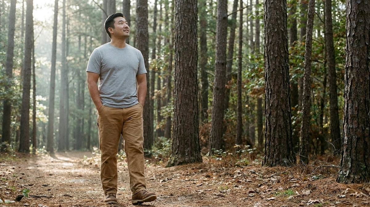 Man in a plain grey tee walking a pine forest trail